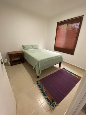 Cozy retreat with a single bed, nightstand, and window with blinds, set against a warm-toned backdrop.