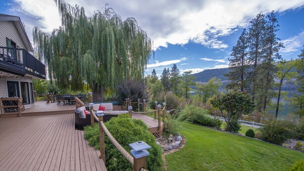 Una terraza con mobiliario exterior, una cerca de madera y vistas a un lago y montañas.