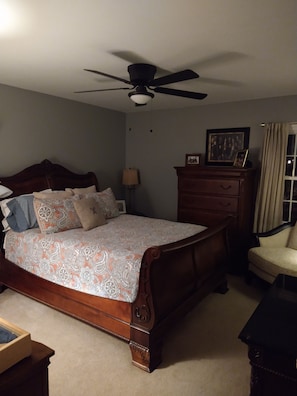 A bedroom with a wooden bed, a ceiling fan, a dresser, a chair, and a framed picture on the wall.