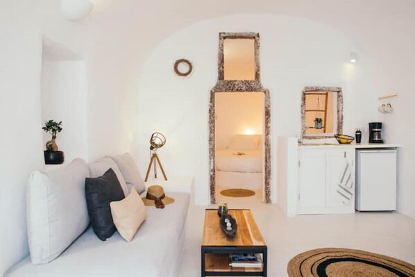 A modern living room with a white sofa, a small coffee table, and a dining area with a white cabinet and a mirror.