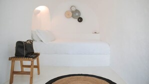 A minimalist room with a white sofa, a wooden stool, and a black bag. - Nykteri Cave | A Terre Cave Villas (Oia)
