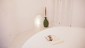 A room with a white round table, a green vase, and a pair of glasses on an open book. - Nykteri Cave | A Terre Cave Villas (Oia)