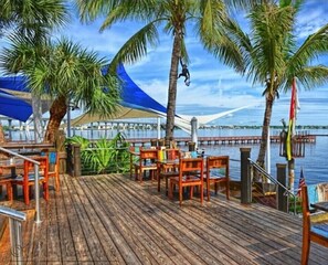 A wooden deck with outdoor seating, palm trees, and a view of the water.