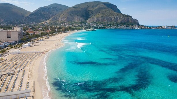 A coastal beach with rows of sun loungers and umbrellas, a clear blue sea, and a mountainous backdrop. - Dante's house, in the historic center of Palermo (Palermo)