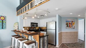 Una cocina moderna con una isla central, taburetes de bar, microondas y refrigerador.