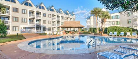 A hotel with a swimming pool, lounge chairs, and a well-maintained garden.