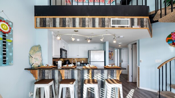 Una cocina moderna con una isla de madera, taburetes de bar y una escalera que lleva a un nivel superior.