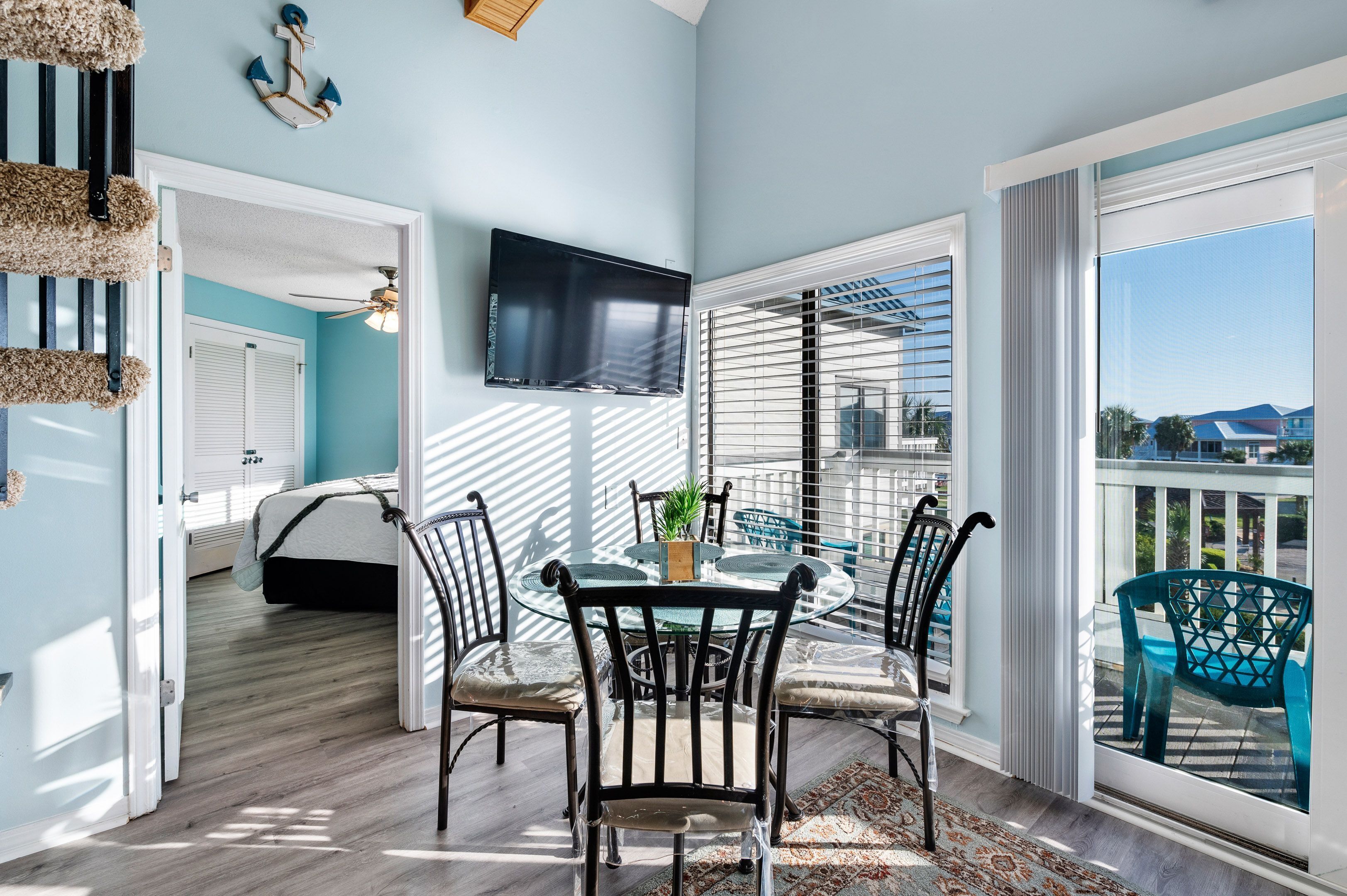 A room with a bed, a dining area with chairs and a table, a TV mounted on the wall, and a balcony with a view.