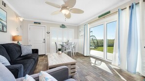 A cozy living room with a ceiling fan, a dining table, and a large sliding glass door leading to a patio.