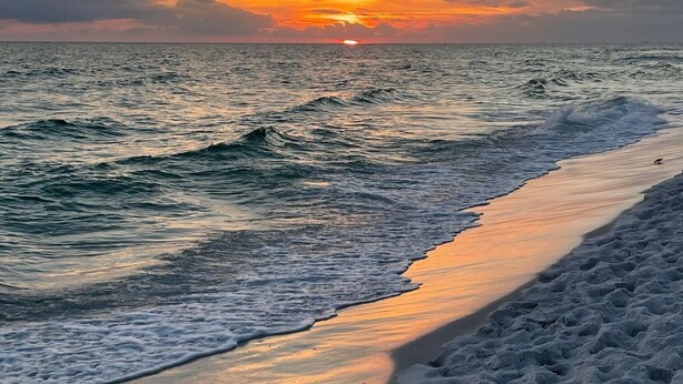 A beach with waves and a sunset.