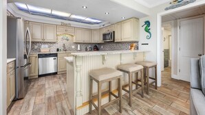 A modern kitchen with a central island, bar stools, and a decorative seahorse wall art.
