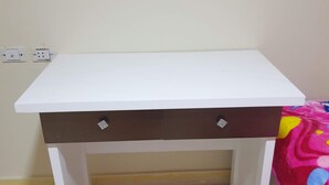 Ein weißer Schreibtisch mit zwei Schubladen und einem braunen Akzent, auf einem Fliesenboden platziert.
