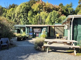 Un café rústico al aire libre con una mesa y bancos de madera, rodeado de follaje y árboles.