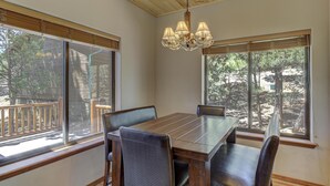 A dining area with a wooden table and chairs, large windows with a view of trees, and a chandelier. - Bison Ridge 4 BR, 4BA Cabin with National Forest access and views! (Show Low)