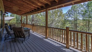 A wooden deck with a covered area, furnished with chairs and a table, overlooking a forested area. - Bison Ridge 4 BR, 4BA Cabin with National Forest access and views! (Show Low)