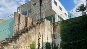 A modern building with a stone facade, a staircase leading to a balcony, and a well-maintained garden area. - Two-story house with pool, well located, 5 minutes from Flamboyant Shopping Center. (Goiânia)