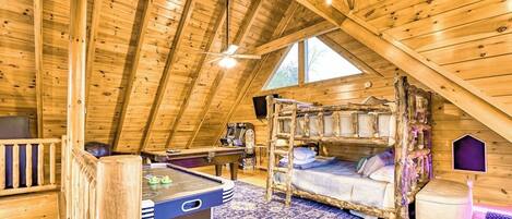 A cozy attic room with a wooden ceiling, a pool table, a bunk bed, and a small desk.