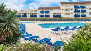 Um hotel com piscina, cadeiras de descanso azuis e um céu azul límpido.