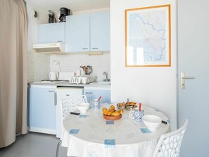 Una cocina compacta con gabinetes azul claro, una encimera blanca y una zona de comedor con una mesa preparada para dos.
