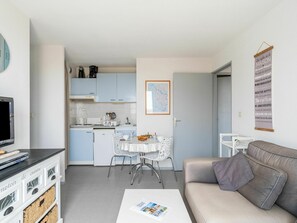 Een kleine leefruimte met kitchenette, eethoek en een bank.