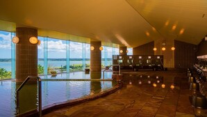 Une piscine intérieure moderne avec vue sur un lac, de grandes fenêtres et un espace d’accueil doté d’un comptoir et de chaises.
