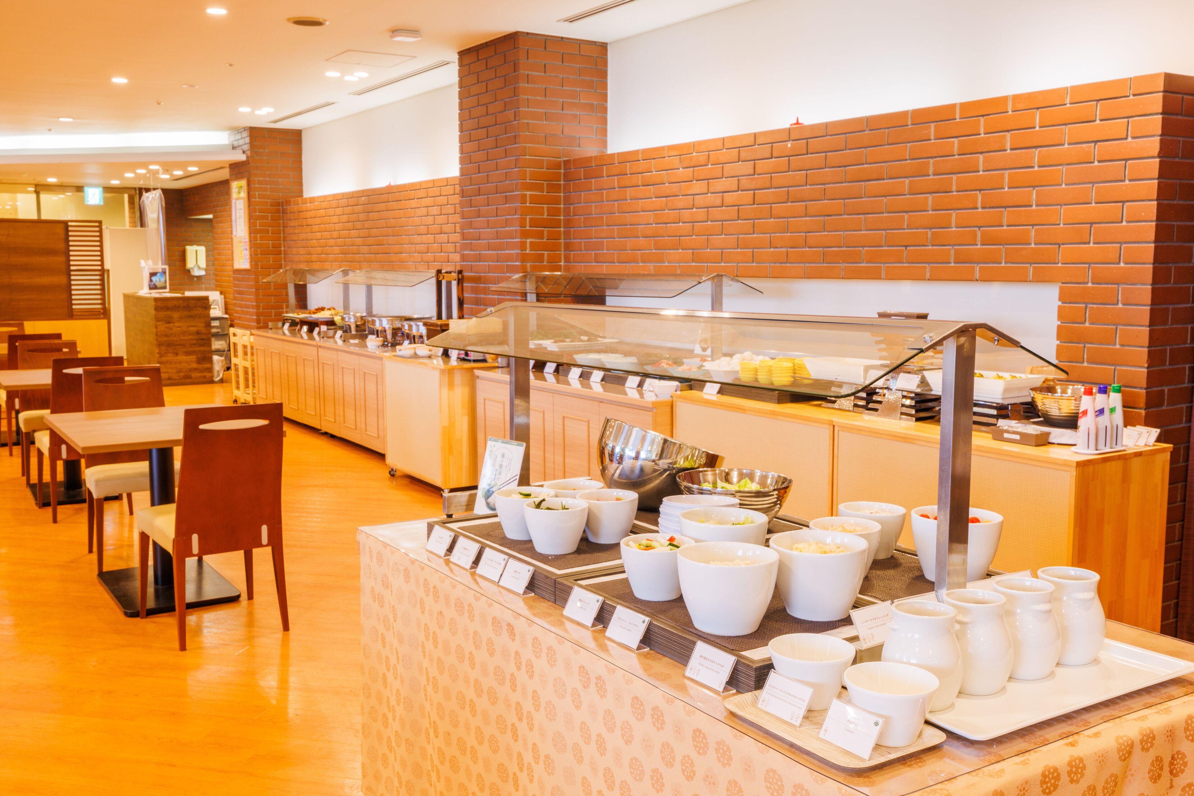 A buffet area with multiple serving stations, a brick wall, and a seating area with tables and chairs.