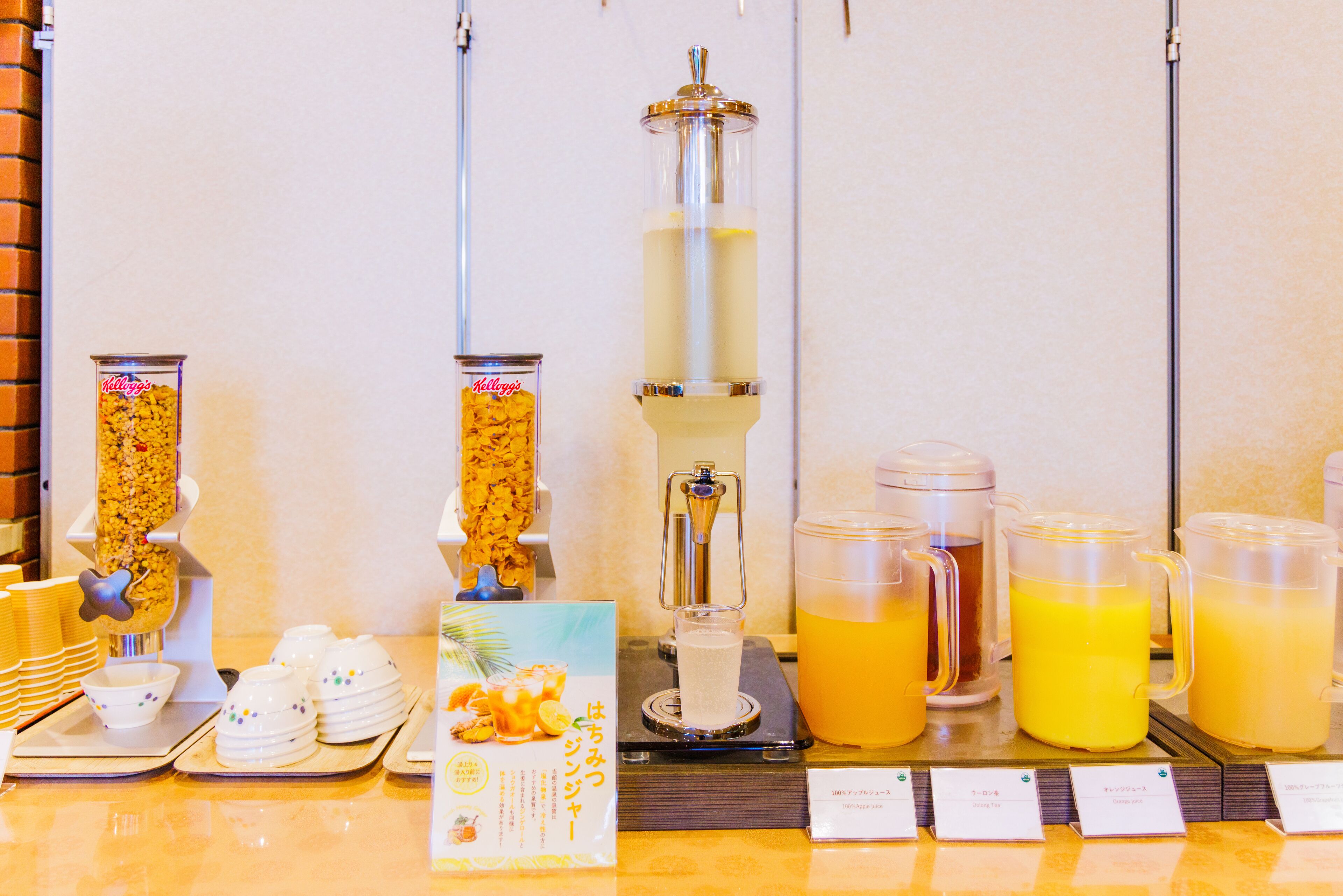 Un buffet proposant une variété de plats et de boissons, notamment un distributeur de céréales, un distributeur de jus et plusieurs carafes de jus d’orange.