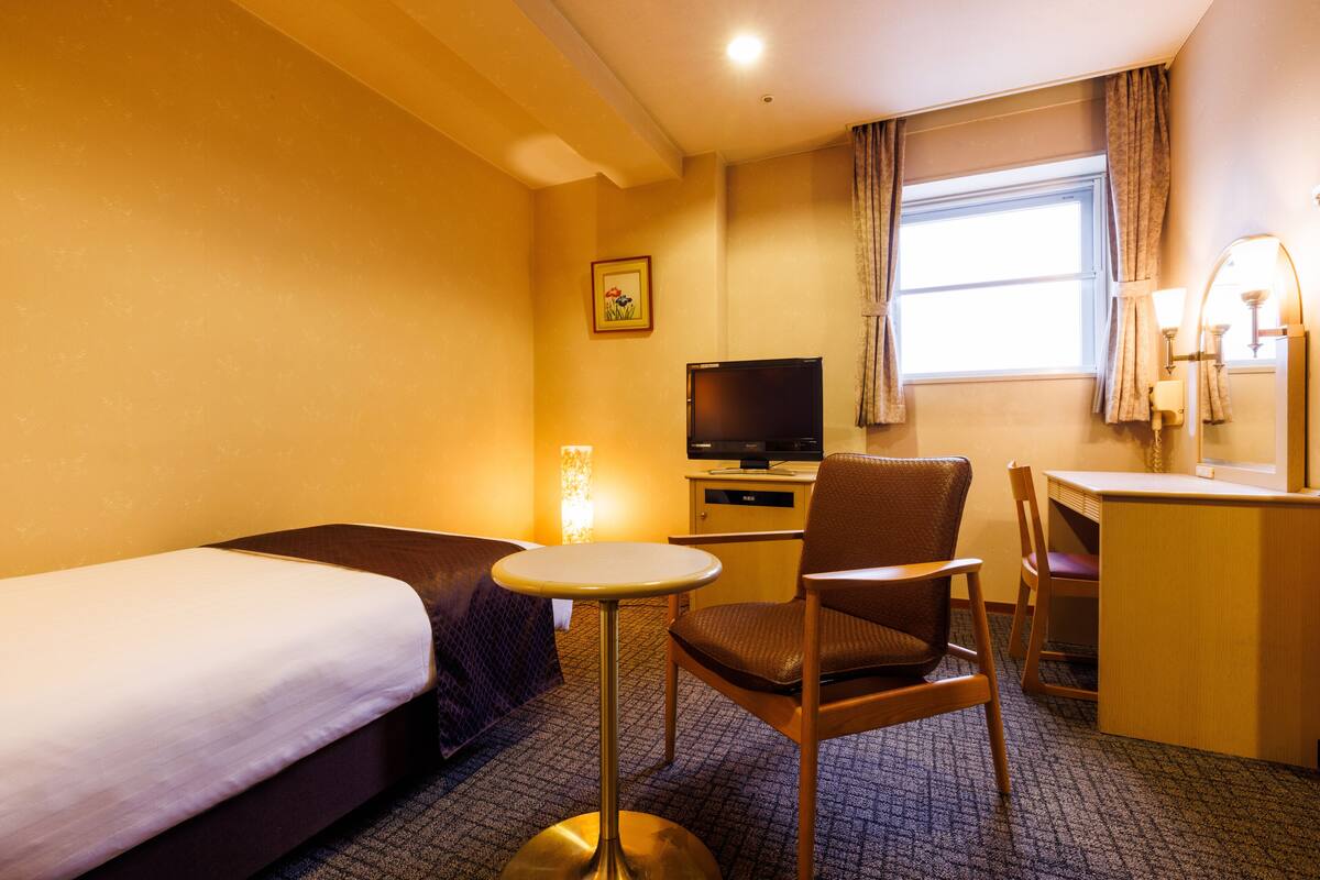 Habitació d'hotel amb dos llits, una taula de treball, una cadira, un televisor i una finestra amb cortines.