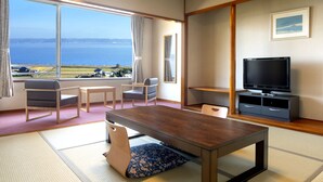 Une pièce avec une table en bois, deux chaises, un téléviseur et une grande fenêtre donnant sur la mer.