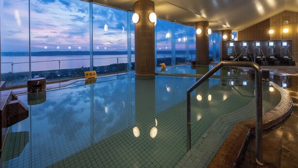 Une grande piscine intérieure avec vue sur le plan d’eau extérieur, des piliers en bois et un espace détente agrémenté d’une rambarde.