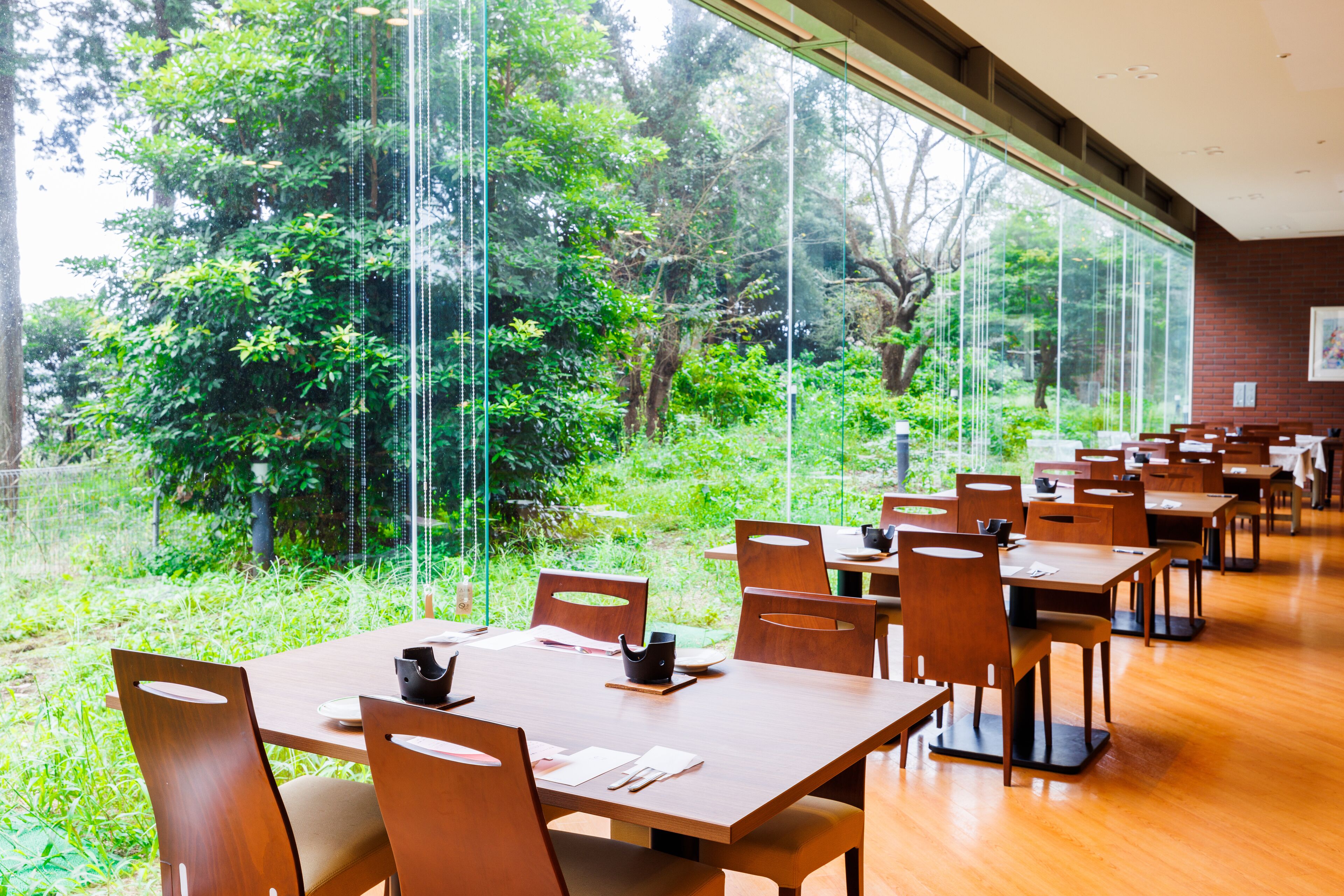 Un comedor con mesas y sillas, ventanas amplias y vista a zonas verdes.