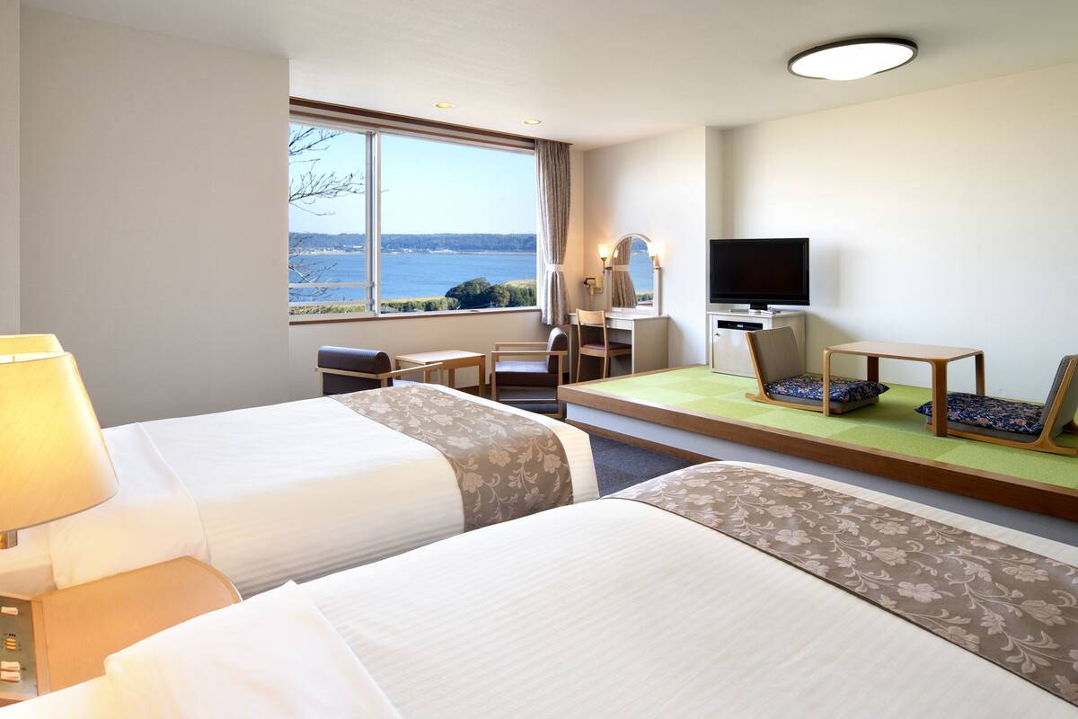 Una habitació d'hotel amb dos llits, un escriptori, una televisió i vista al mar.
