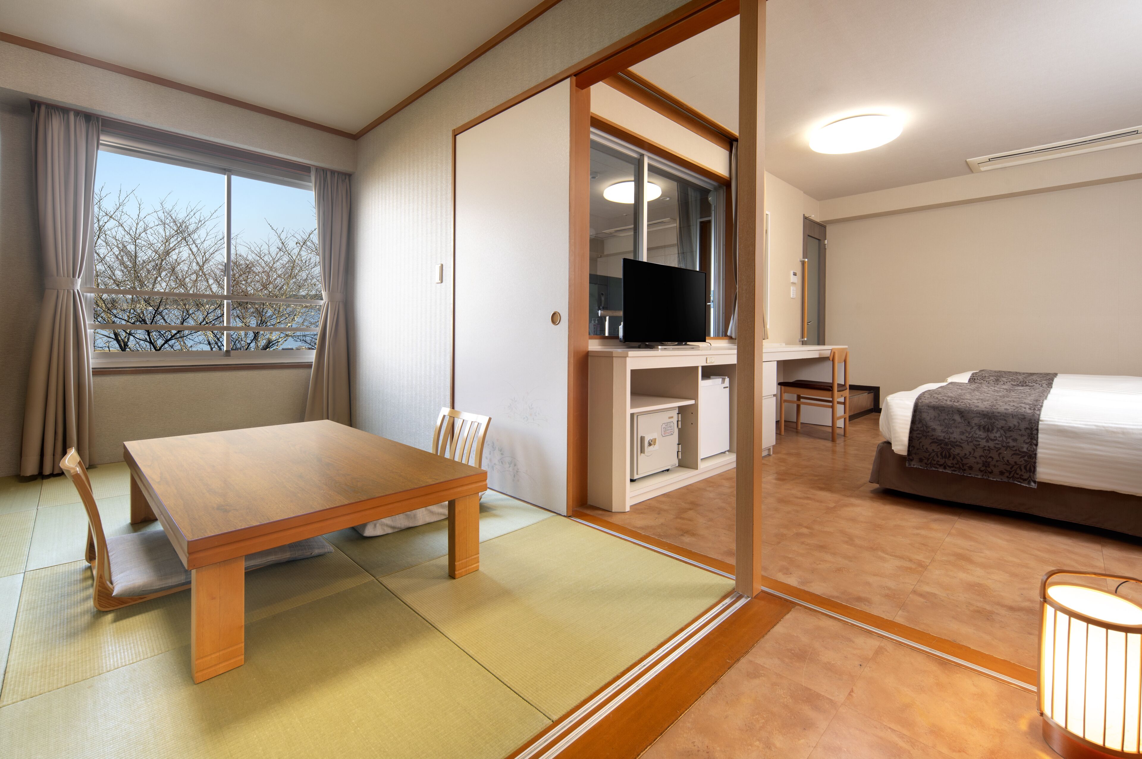 Une chambre d’hôtel avec un bureau en bois, un lit, une télévision et une vue sur les arbres par la fenêtre.