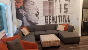 A modern living room with a sectional sofa, ottoman, and a large wall mural with the text "LIFE IS BEAUTIFUL". - Discount for a 30 day stay! Luxury 4 all queen beds. Walk to the harbor + views (San Pedro)