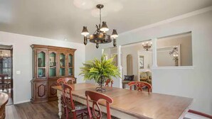 Uma sala de jantar com mesa de madeira, cadeiras vermelhas, um armário grande e um candelabro.