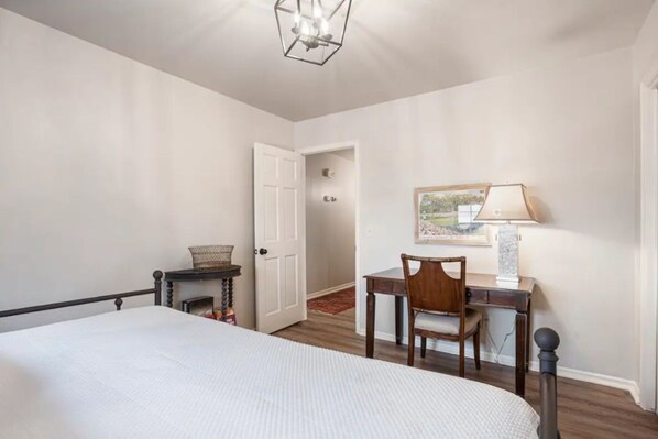 Quarto com cama, escrivaninha, cadeira, luminária e porta que dá para outro cômodo.