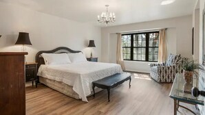 Quarto com uma cama grande, mesas de cabeceira, um banco, janela com cortinas e um lustre.