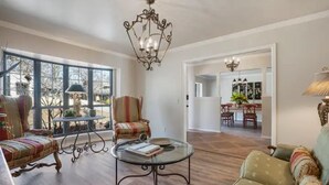 Uma sala de estar espaçosa com uma mesa de centro de vidro, poltronas listradas e um lustre.
