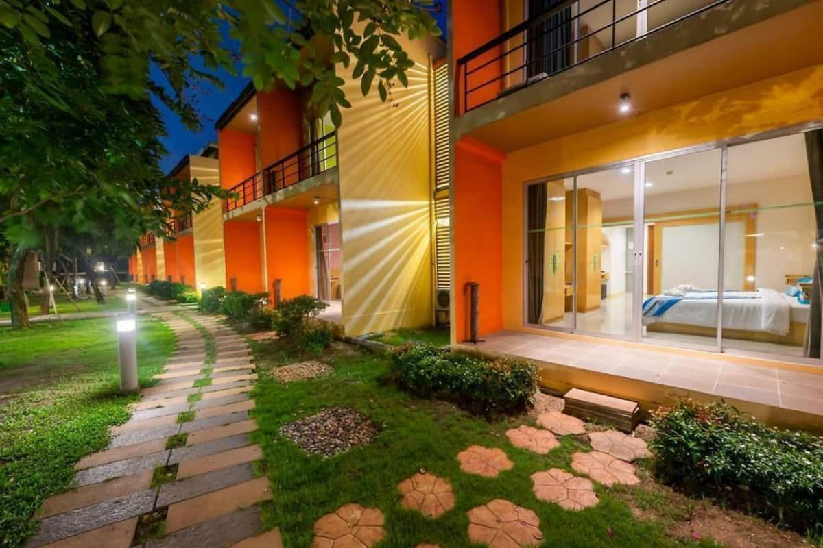 A hotel with a modern design, featuring a glass facade, a well-maintained garden with a stone pathway, and a balcony with a railing.