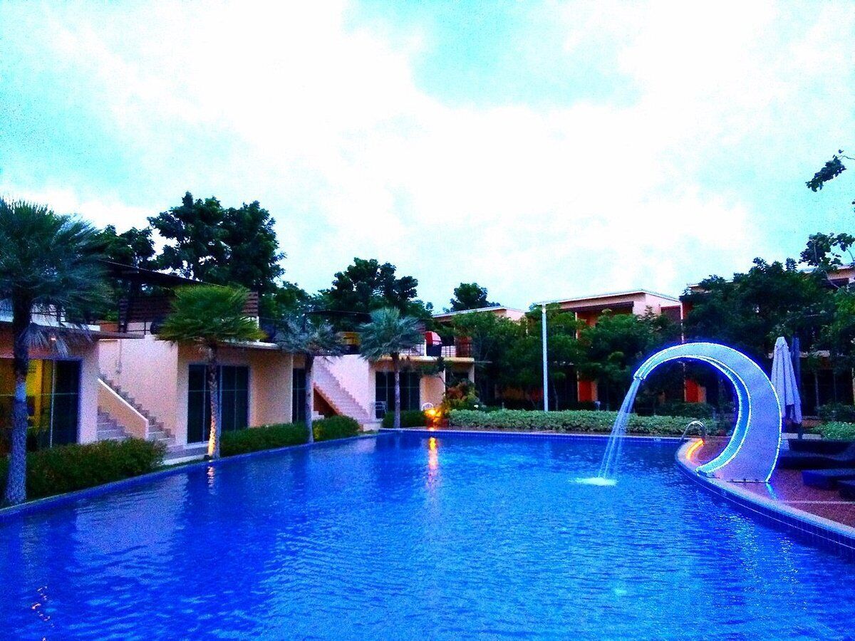 Piscina com um elemento aquático, rodeada por palmeiras e edifícios.