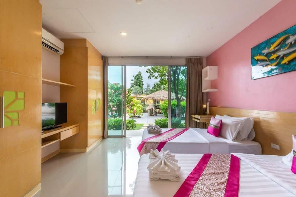 A hotel room with two beds, a TV, and a view of a garden and thatched-roof structure.
