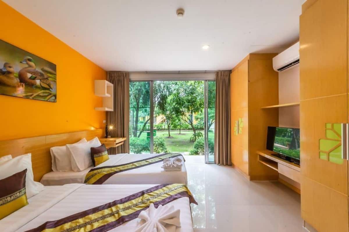 A hotel room with two beds, a television, and a view of a garden.