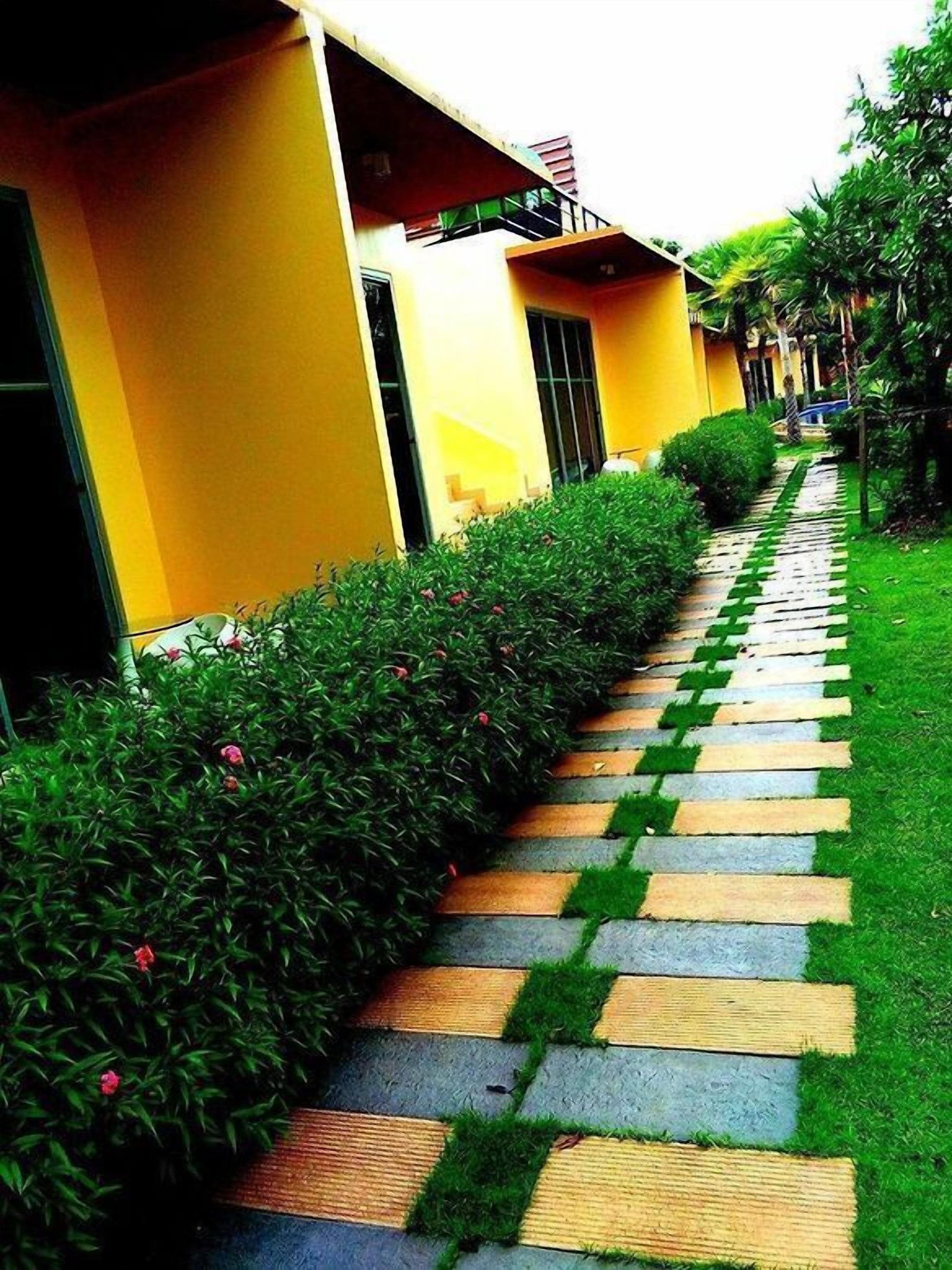 A pathway leading to a yellow building with a covered entrance and a small garden area.