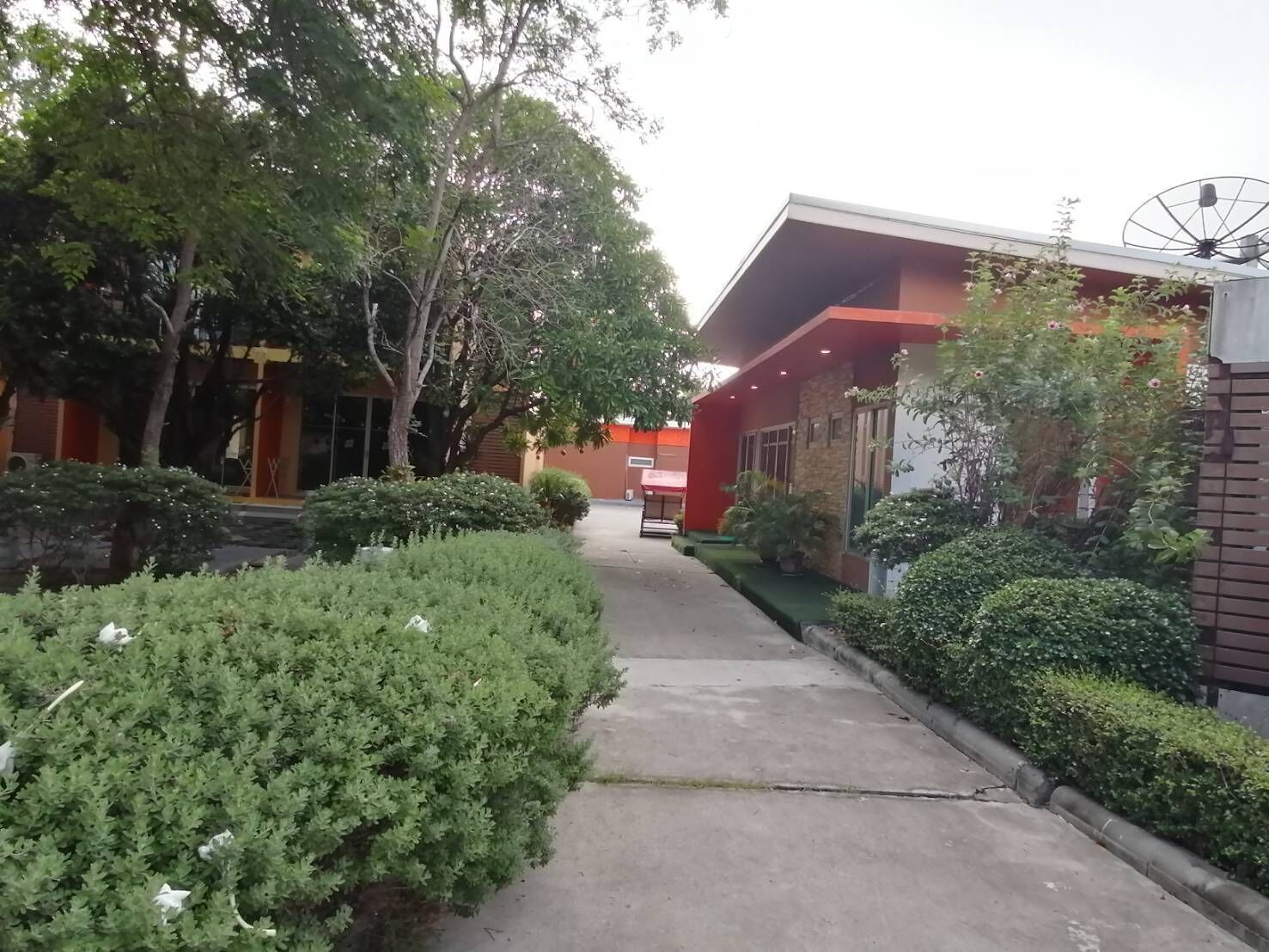 Un chemin menant à un bâtiment à la façade rouge, entouré de verdure et d’arbres.