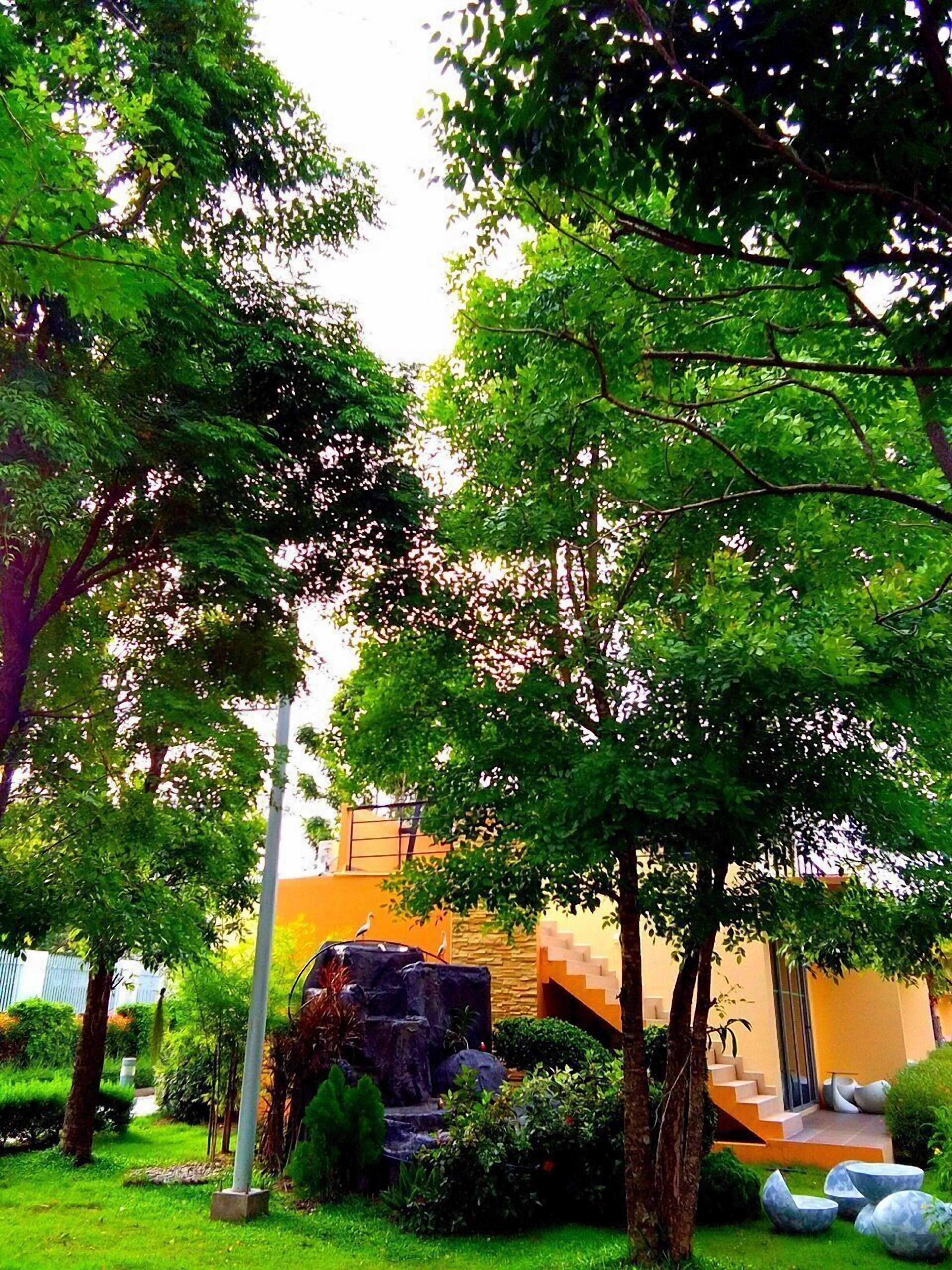 Un exuberante jardín con una cascada de piedra, un edificio moderno con una escalera y un cielo despejado.