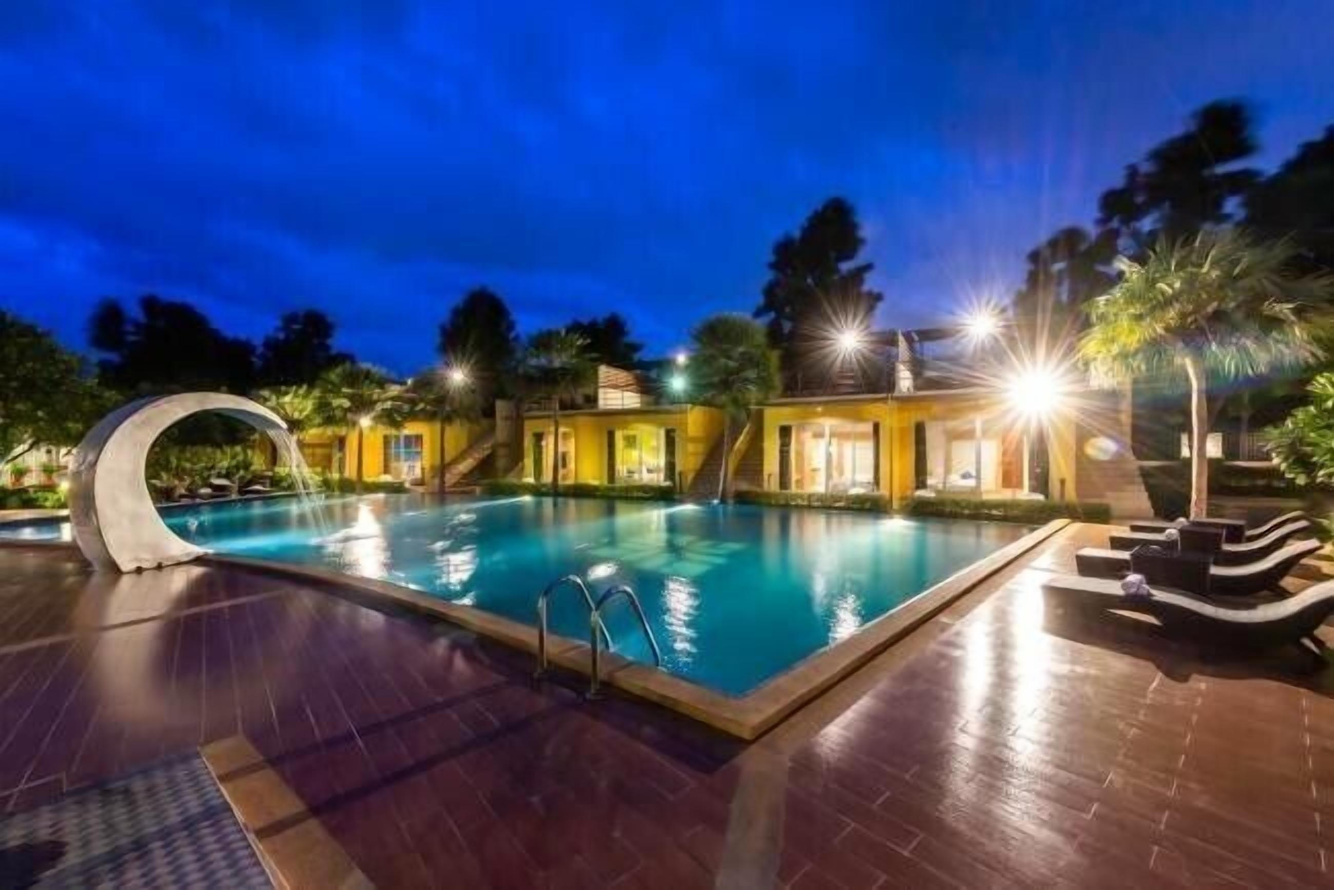 A swimming pool with a curved edge, surrounded by lounge chairs and a small waterfall feature.