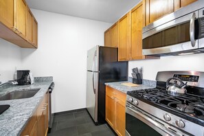 A kitchen with wooden cabinets, a stainless steel refrigerator, a microwave, a gas stove, and a sink.
