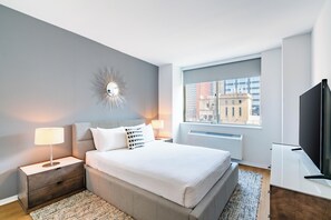 A modern hotel room with a large bed, bedside tables, a TV, and a window with a city view.