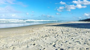 Ein weiter Sandstrand mit sanften Wellen, blauem Himmel und vereinzelten Wolken.