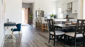 Une cuisine moderne avec des meubles blancs, un îlot central doté de chaises et un coin repas avec une table en bois foncé.